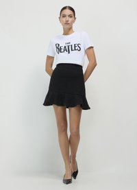 T-shirt bianco con grafica nera "The Beatles", abbinato a una gonna nera a balze testurizzate e tacchi a punta neri.