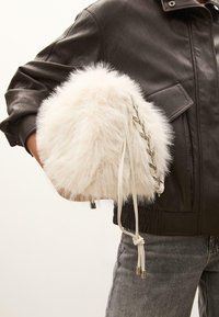 Plysset hvidt faux fur håndtaske med en flettet hvid rem og sølv hardware detaljer. Stylet sammen med en mørk læderjakke og grå jeans.