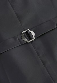 Un tissu noir avec une texture lisse présente une fermeture à boucle métallique à la taille, complétant le design structuré.