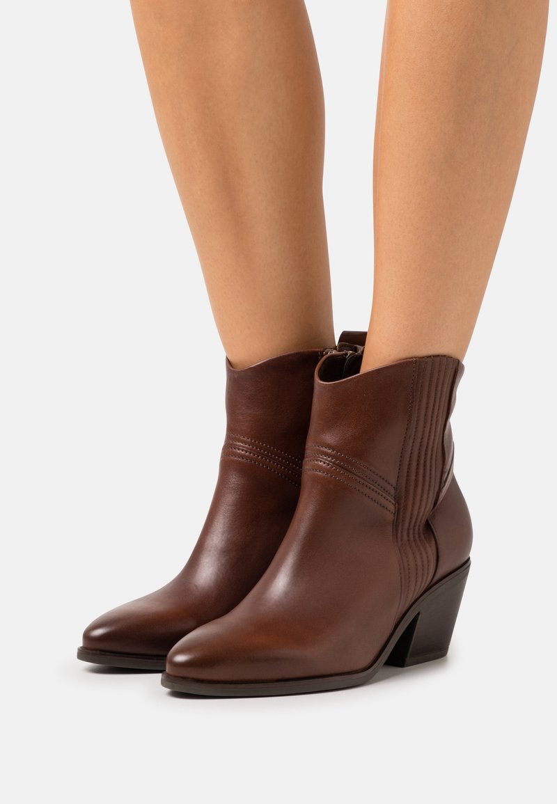 Bottines en cuir marron avec un bout pointu et un talon bas et incliné. Des coutures verticales soulignent les côtés, ajoutant de la texture au design.