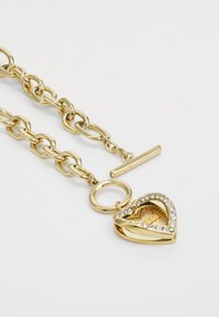 Bracciale in oro con ciondolo a forma di cuore decorato con cristalli trasparenti, finitura testurizzata e chiusura a moschettone.