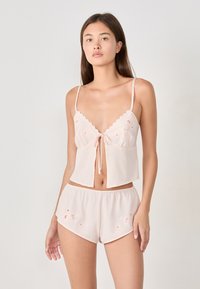 Set di pigiama corto di colore rosa chiaro, composto da una cima ricamata corta con scollatura a onda e pantaloni corti abbinati con dettagli floreali.