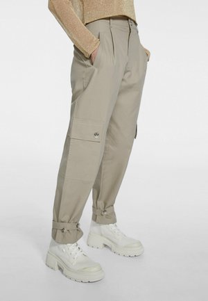 Beige cargobroek met gepofte klepzakken en verstelbare manchetten, gecombineerd met witte chunky veterlaarzen tot aan de enkel.