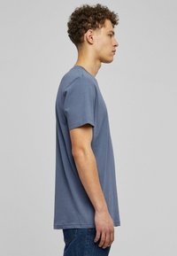 Slim-fit blue cotton t-shirt with short sleeves, crew neckline, and straight hem, displayed on a model in profile view.
