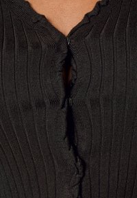 Cardigan nero a costine con chiusura a bottone sul collo, caratterizzato da un delicato bordo ondulato lungo il colletto e un tessuto testurizzato.