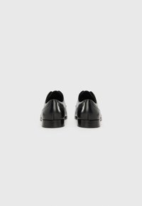 Zapatos de vestir de cuero negro con un acabado suave, punta redondeada y tacón bajo; diseño minimalista, sin herrajes o patrones visibles.