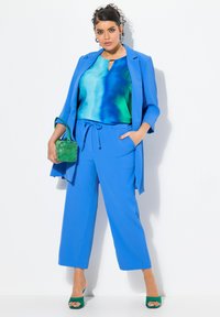 Traje pantalón azul a medida con blusa en degradado de azul claro a verde. Un bolso verde y sandalias de tacón a juego completen el look.