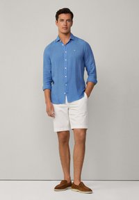 Světle modrá košile s dlouhým rukávem a knoflíkovým zapínáním, bílé šortky, hnědé nazouvací boty. Jednoduchý design, hladká textura a ležérní střih.