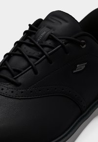 Baskets en cuir noir avec lacets noirs, détails perforés, languette rembourrée portant l'inscription "Prestige" et petit logo "S" embossé sur le côté.