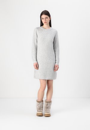 Robe tricotée grise à manches longues, col rond et texture côtelée. Associée à des bottes beige en fourrure pour la chaleur et le confort.