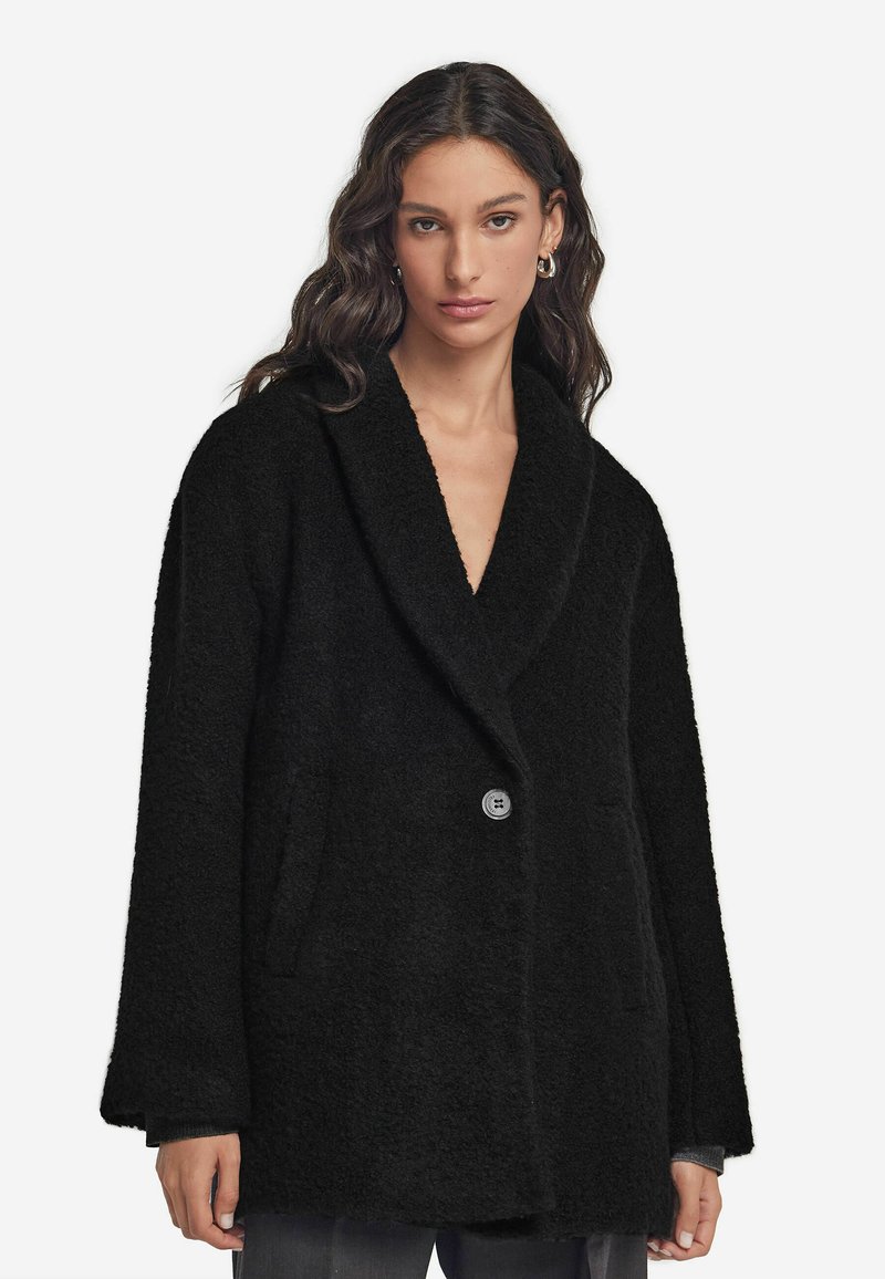 Czarny, oversize płaszcz wykonany z teksturowanej tkaniny. Posiada szeroki kołnierz, zapięcie na jeden guzik i kieszenie boczne.