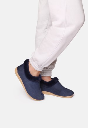 Navy blue slippers with a textured upper and fluffy faux fur collar, paired with light grey joggers featuring elastic cuffs.