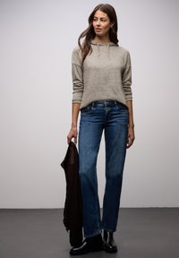 Jasnoszara bluza z kapturem o miękkiej fakturze, zestawiona z niebieskimi dżinsami o prostych nogawkach, czarnymi botkami za kostkę oraz brązową kurtką trzymaną w ręce.