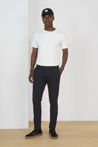 Camiseta blanca de manga corta, pantalones ajustados azul marino y zapatillas negras. La gorra negra tiene un logotipo cuadrado. Diseño minimalista con colores sólidos.