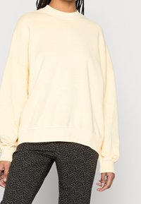 Jasnożółta, oversizeowa bluza z okrągłym dekoltem i opuszczonymi ramionami, wykonana z miękkiego, gładkiego materiału. Dopasowane spodnie w tym samym wzorze.