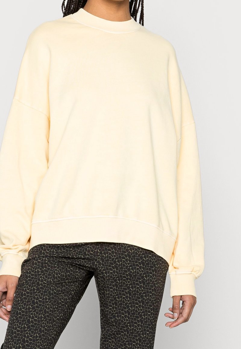 Jasnożółta, oversizeowa bluza z okrągłym dekoltem i opuszczonymi ramionami, wykonana z miękkiego, gładkiego materiału. Dopasowane spodnie w tym samym wzorze.