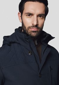 Granatowa pikowana kurtka z kołnierzem z sztucznego futra, z zapięciem na zamek i guziki, kieszeniami po bokach oraz fakturowanym materiałem.