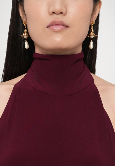Vyno raudonos spalvos aukštu kaklu megztinis su lygiu paviršiumi, derinamas su auksiniais auskarais su perlu ir sudėtingu orbitos dizainu.