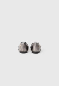 Metallic gray ballet flats with a rounded toe, featuring a small bow accent and a flat black sole. Smooth, shiny texture with logo detail.