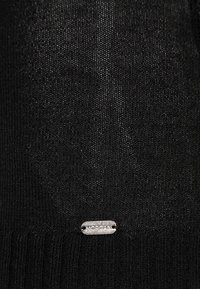 Schwarzer Strickstoff mit einem kleinen silbernen Etikett, auf dem "MORGAN" eingraviert ist, das nahe der unteren Mitte angebracht ist.