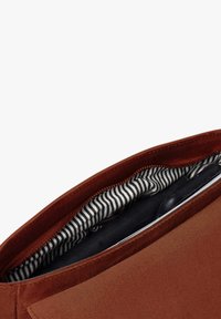 Braune Wildledertasche mit einem Reißverschluss, ausgestattet mit einem gestreiften Futter in Schwarz und Weiß, das den Innenraum zeigt.