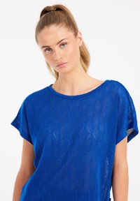 Mėlynas megztinis su laisvu sijonu, trumpomis rankovėmis, apvalia iškirpte ir rombo formos raštu. Medžiaga yra lengva ir tekstūruota.