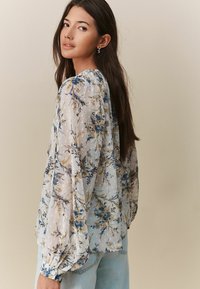 Bluză transparentă cu imprimeu floral, cu mâneci lungi și decolteu plisat în bleu deschis, cu flori galbene și bleumarin și o țesătură texturată.