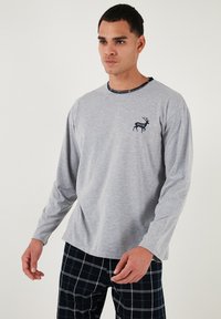 Camisa de manga larga gris con un cuello azul marino, que presenta un pequeño gráfico de un ciervo azul marino en el pecho, combinada con pantalones de pijama a cuadros azul marino.