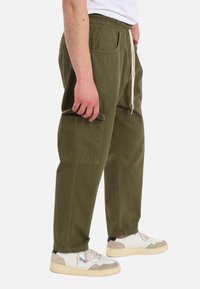 Pantaloni di cotone verdi con vita elastica, lacci regolabili e tasche laterali. Presenta una tasca cargo singola sulla coscia.