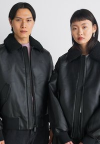 Μαύρες δερμάτινες αεροπορικές τζάκετ με γούνινες κολάρες, διαθέτοντας μπροστινούς φερμουάρ, πλαϊνές τσέπες και χαλαρούς μανίκους. Απλό λογότυπο στην περιοχή του στήθους.