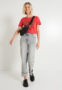 Camiseta roja con un corazón de estampado de leopardo, jeans gris de talle alto, bolsa negra de mano con tachuelas y zapatos negros gruesos.
