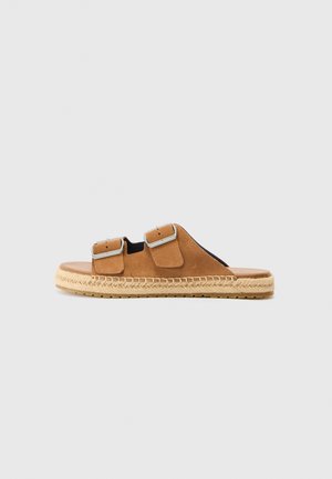 Sandale slide en daim marron avec deux brides à boucle réglables et semelle en jute tissée sur fond neutre.
