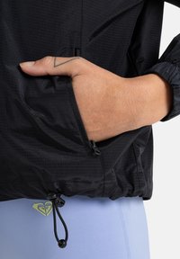 Black lightweight jacket with textured fabric, elastic cuffs, and a pocket. Features an adjustable drawstring at the hem.
