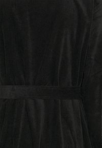 Tessuto di velluto a coste nero con una superficie texture, dotato di una cintura intrecciata in vita. Il design include righe verticali e una finitura liscia.