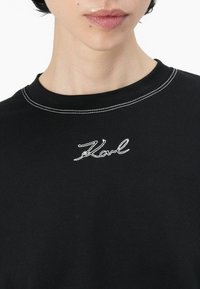 Svart bomull T-skjorte med rund hals, utstyrt med hvite kontrastsømmer og en brodert "Karl"-logo på brystet.