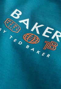 Tyrkysová tkanina s výrazným bielym a oranžovým logom. Text obsahuje "BAKER," "by TED BAKER," a ikonu glóbu. Mäkka textúra, neformálny dizajn.