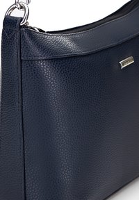 Námořnická texturovaná kožená taška s hladkým vrškem, stříbrnými kovovými detaily a zapínáním na zip. Má elegantní, moderní tvar.