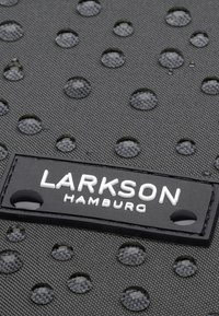 Black textured fabric with raised circular dots and water droplets. Features a rectangular label with white lettering reading "LARKSON HAMBURG."