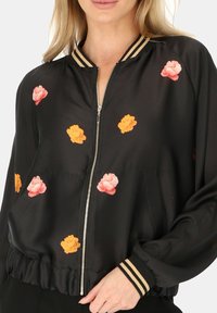 Czarna satynowa kurtka bomberka z kwiatowym haftem w odcieniach różu i pomarańczu. Posiada srebrny zamek błyskawiczny oraz prążkowany kołnierzyk i mankiety.