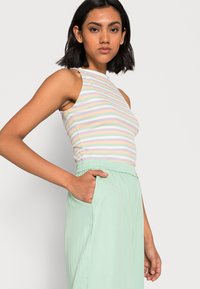 Top sem mangas listrado em cores pastel (rosa, amarelo, lavanda) combinado com calças largas verde claro com uma cintura elástica e bolsos laterais.