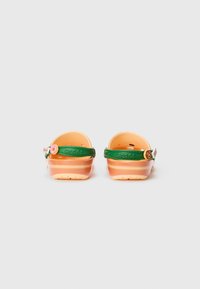 Orange und beige Plastik-Clogs mit einem grünen verstellbaren Riemen, der einen dekorativen Charme trägt und runde Löcher zur Belüftung bietet.