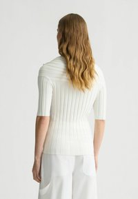 Top a coste bianco con maniche corte, caratterizzato da un colletto alto e una vestibilità slim. La texture è liscia, con righe verticali su tutta la superficie.