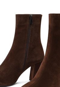 Botas de tobillo de ante marrón con cremallera lateral, tacón cuadrado, textura suave y un diseño elegante y minimalista.