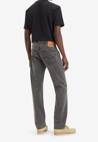 Mörkgrå jeans med avslappnad passform, med dubbla bakfickor och en brun läderlapp i midjan. Matchas med en svart t-shirt.