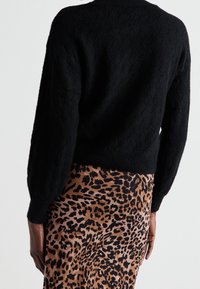 Svart stickad tröja med ett texturerat, diamantmönster och ribbade ärmar, i kombination med en leopardmönstrad kjol i varma toner.