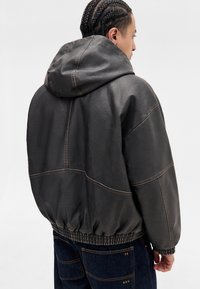Grå faux læderjakke med hætte, elastisk talje og kontrastsyning. Tyk materiale med en tekstureret overflade.