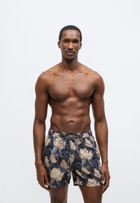 Čierne plavkové šortky s kvetinovým vzorom v béžovej a zelenej farbe. Elastický pás so sťahovacou šnúrkou, krátky strih a ľahká tkanina.
