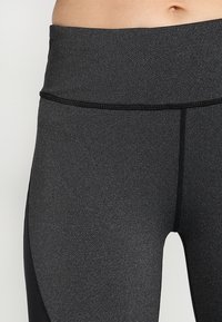 Detailní záběr na střed těla osoby oblečené v tmavě šedých sportovních legínách s vysokým pasem a černým šitím.