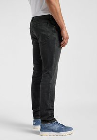 Zwarte denim jeans met een slim fit, voorzien van achterzakken en subtiele vervaging. Gecombineerd met blauwe textuur sneakers.