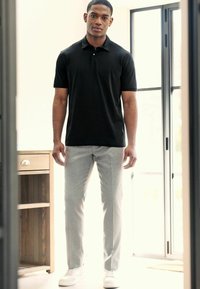 Polo negro de manga corta combinado con pantalones de vestir gris claro. El conjunto se completa con zapatillas blancas y un sencillo botón plateado como acento.